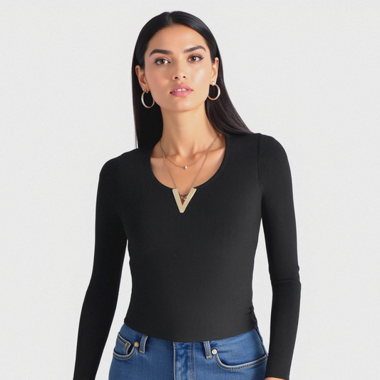 Woman wearing an accessorized black long-sleeve top with a geometric neckline and blue jeans on a white background